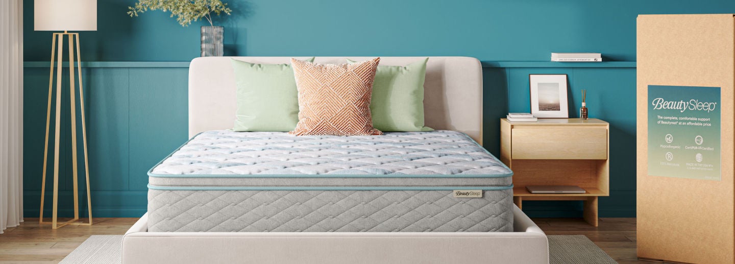 BeautySleep Pillowtop Mattress sitting in a grey bed frame with 3 pillows on top of it.
