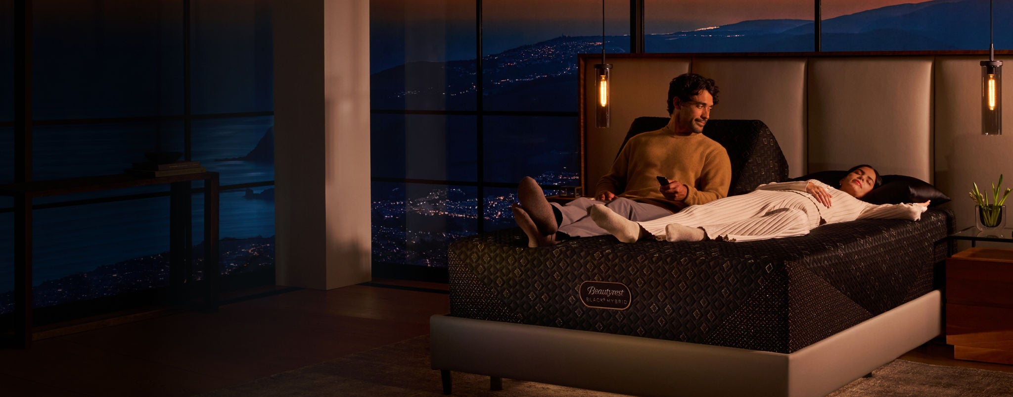 Woman and man laying on a Beautyrest split mattress with the man siting up on the left side of the adjustable base and the woman laying flat on her back