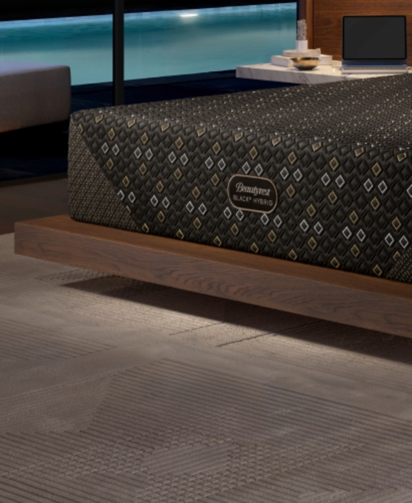 Corner of a Beautyrest Black Hybrid XCS mattress sitting on top of a brown bedframe