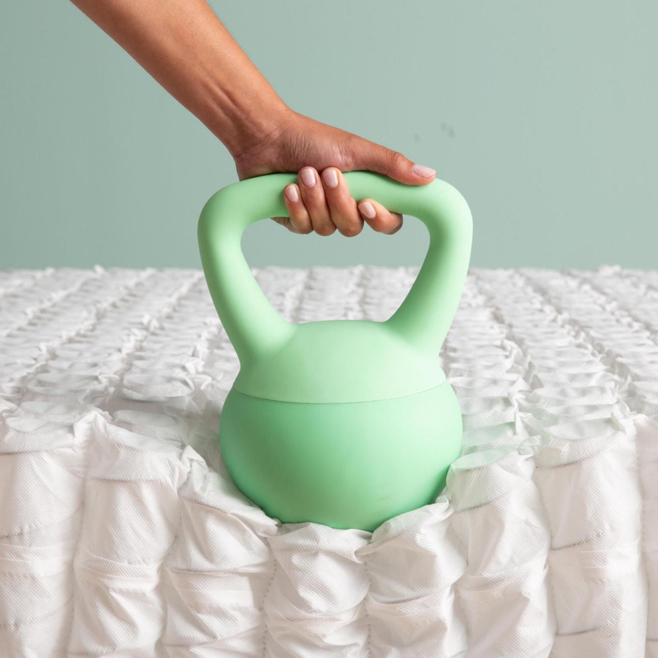 Woman holding a green cow bell weight placed upon the innersprings of the Beautysleep mattress