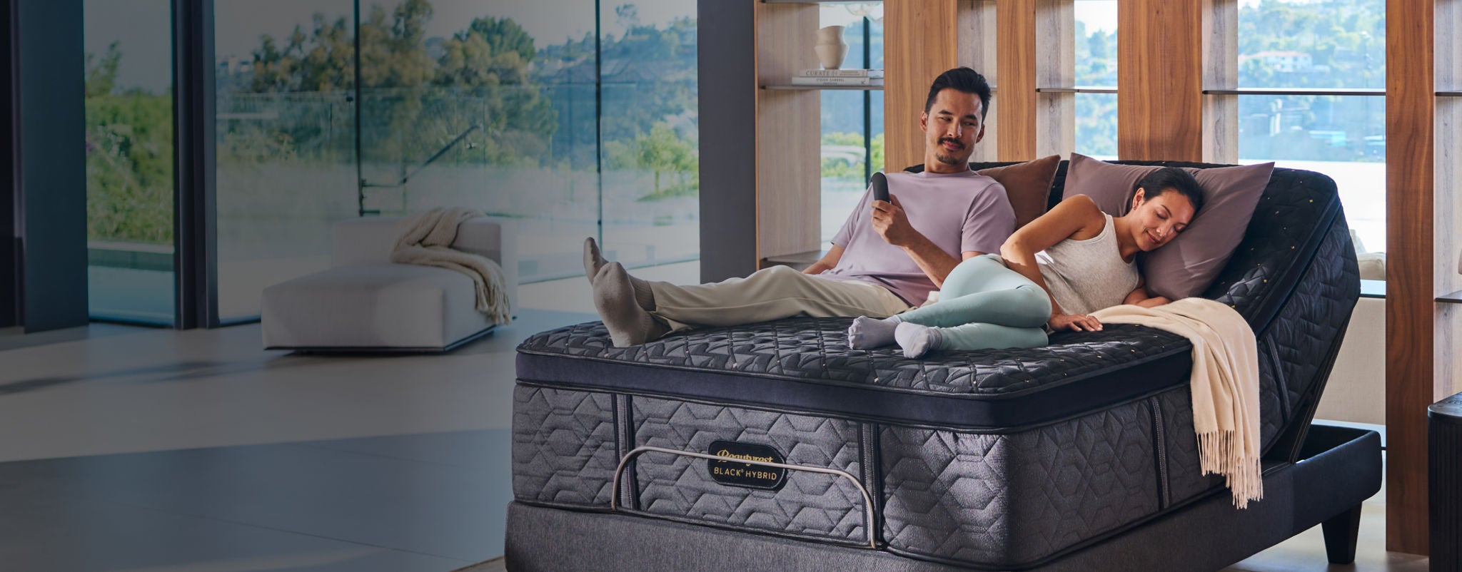Woman and man sitting on a Beautyrest Black Hybrid mattress on an adjustable base slightly elevated.