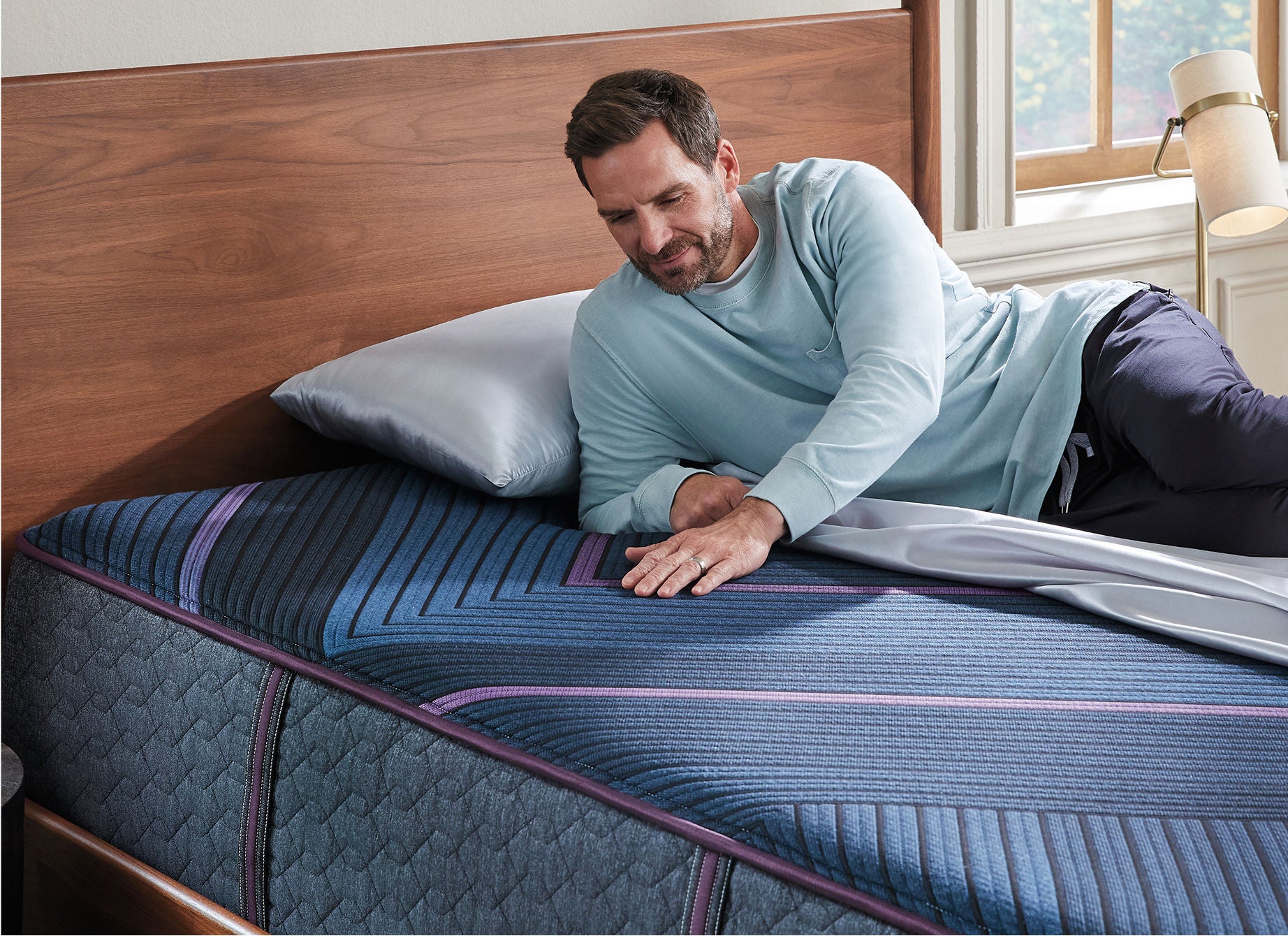 Man laying on top of a Beautyrest World Class mattress rubbing the top of the mattress