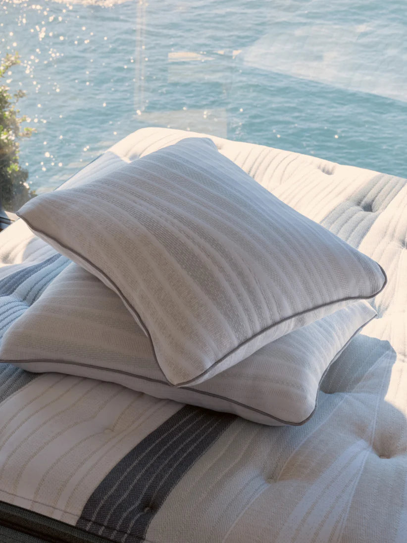 Two white-striped pillows resting on a mattress with a serene ocean view in the background.