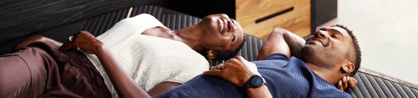 A couple happily laying down on a Beautyrest Black mattress on their backs and relaxing.