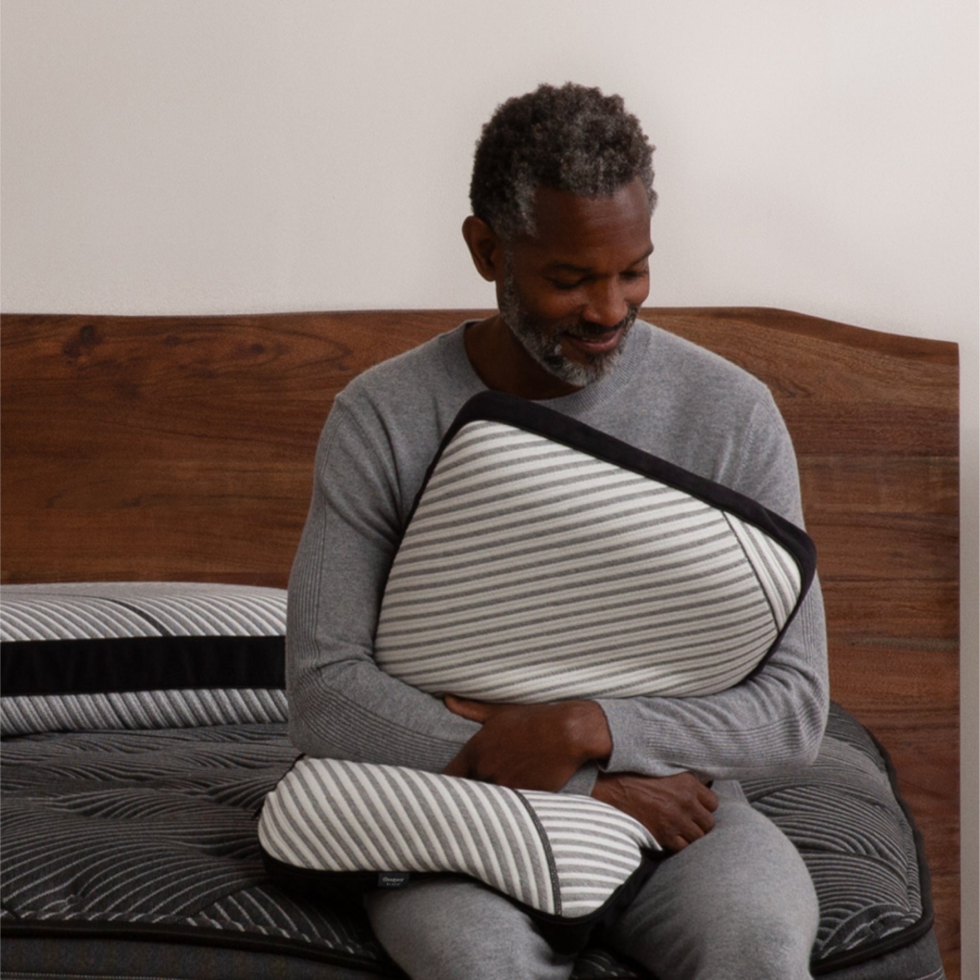 A man sitting on a bed, squeezing the Beautyrest Black Luxury Foam Pillow
